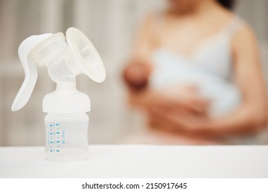 Breast Pump With Breast Milk Against The Background Of A Mother Holding Child.