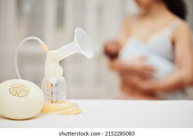 Breast Pump With Breast Milk Against The Background Of A Mother Holding Child.