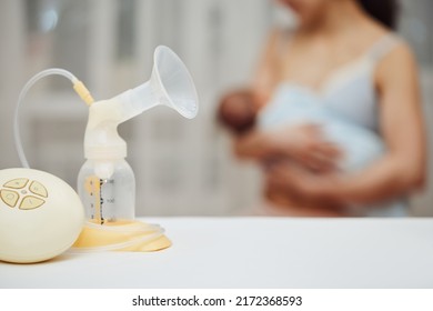 Breast Pump With Breast Milk Against The Background Of A Mother Holding Child.