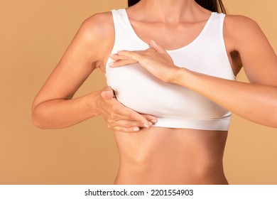 Breast self-screening concept. Young woman in white bra making checkup for cancer prevention, beige studio background, closeup, cropped