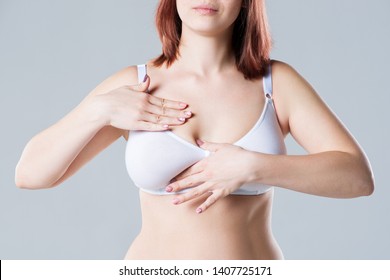 Breast test, woman examining her breasts for cancer, big natural boobs on gray background, close-up studio shot