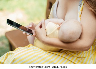 Breastfeeding Apps For New Parents, Moms. Young Mother Holding Newborn In Embrace And Look Into Smartphone. Close Up Of Mother Breastfeeding Her Child Outdoor With Cell Phone