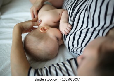 Breastfeeding A Baby For 6 Months, Mother Gently Embraces A Baby. Top View On Real Bed