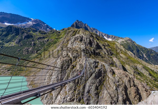 Breath taking view of the Trift bridge, a\
suspension bridge over the Triftsee, glacier, in Gimsel on Bernese\
Oberland, Switherland.