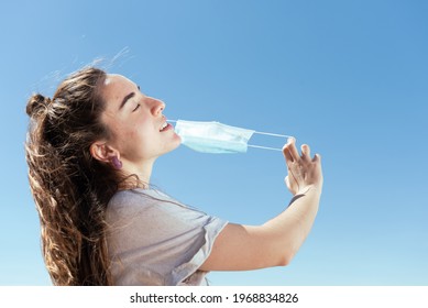 Breathing And Feeling Free During Coronavirus Pandemic Concept. Young Woman Removing A Protective Surgical Mask.