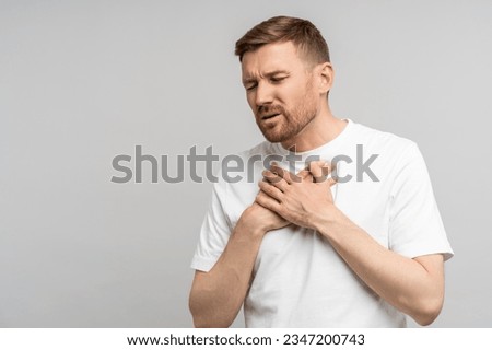 Breathing problem. Man holds on to chest suffering from heartburn. Caucasian young guy suffers from pain in sternum. Unbearable pain tearing apart chest, burning inside and suffering, acute discomfort
