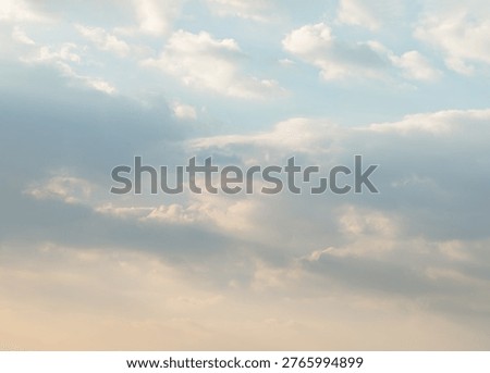 A breathless celestial canvas transitions from soft cerulean to a warm apricot glow. Wispy, cotton-like clouds drift through the upper reaches, their luminous edges softened by a gentle light. Denser, lavender-tinted layers add depth and stately movement to the atmosphere, while the lower quadrant is bathed in a delicate wash of amber and gold. Diffused sunbeams filter through a dreamlike mist, blurring the line between the heavens and the earth in a masterpiece of tranquility.