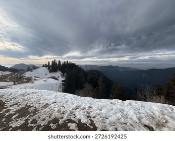 Breathless panoramic view of snow-capped mountains under a dramatic cloudy sky at sunset. Beautiful winter landscape featuring rolling hills covered in white snow, pine tree forests, and a golden horizon. Scenic Himalayan mountain range view during a cold winter evening, perfect for nature and travel backgrounds