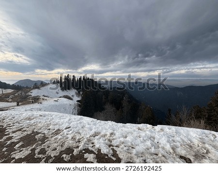 Breathless panoramic view of snow-capped mountains under a dramatic cloudy sky at sunset. Beautiful winter landscape featuring rolling hills covered in white snow, pine tree forests, and a golden horizon. Scenic Himalayan mountain range view during a cold winter evening, perfect for nature and travel backgrounds
