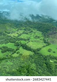An breathtaking aerial view captures a patchwork of vibrant green fields and dense forests stretching across rolling hills under a hazy sky, showcasing pristine nature.