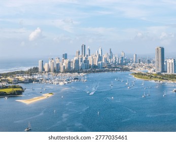 A breathtaking aerial view capturing the iconic Gold Coast skyline, bustling waterways filled with sailing boats, and serene coastal beauty on a sunny day.