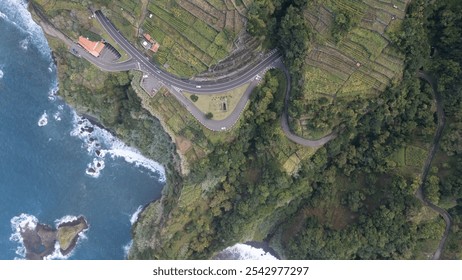 A breathtaking aerial view capturing a winding coastal road, lush green hills, and a dramatic ocean shoreline. The landscape offers a beautiful contrast between nature and human-made structures. - Powered by Shutterstock