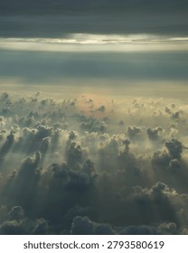 A breathtaking aerial view of dramatic clouds illuminated by soft sunlight streaming through the sky. Ethereal sun rays pierce the cloud formations, creating a serene and majestic atmosphere. Perfect for themes of nature, weather, spirituality, tranquility, freedom, heavenly landscapes, and environmental backgrounds.