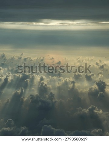 A breathtaking aerial view of dramatic clouds illuminated by soft sunlight streaming through the sky. Ethereal sun rays pierce the cloud formations, creating a serene and majestic atmosphere. Perfect for themes of nature, weather, spirituality, tranquility, freedom, heavenly landscapes, and environmental backgrounds.