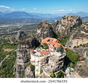 A breathtaking aerial view of monasteries perched atop towering rock formations, set against a vast landscape of mountains and valleys. The ancient structures with red-tiled roofs stand in harmony wit - Powered by Shutterstock