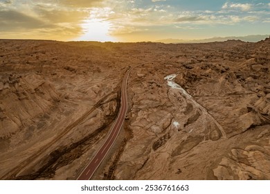 A breathtaking aerial view of a rugged desert canyon landscape at golden hour, showcasing dramatic rock formations, sandy terrain, and a winding road under a clear sky. - Powered by Shutterstock