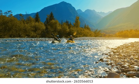 Una impresionante vista Aéreas muestra a dos kayakistas navegando por un río rápido, rodeados de impresionantes montañas y exuberantes bosques. Los kayakistas, uno en un kayak verde y el otro en uno amarillo.