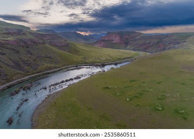 A breathtaking aerial view of a tranquil river winding through a wide, expansive valley surrounded by rolling hills and dramatic skies in Idaho - Powered by Shutterstock