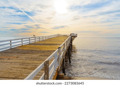 Breathtaking beauty of a sunrise over Malibu Pier in California. Calm ocean waters reflect soft hues of pink and orange, seagulls rest peacefully on pier. Stillness and beauty of the natural world.