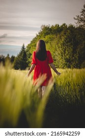 Breathtaking Candid Portrait Of A Brunette Aged 20-24 In A Loose Red Dress In A Cornfield, Smiling Naturally. Fashion Vintage Style. Natural Beauty Of A Brown Haired European Woman.