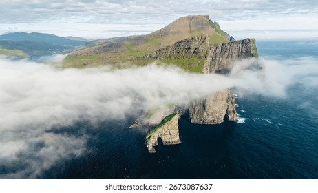Breathtaking cliffs rise dramatically from the North Atlantic, enveloped in a soft mist, creating a mystical atmosphere in the Faroe Islands. Drangarnir cliffs