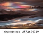 A breathtaking display of iridescent and nacreous clouds fills the sky. Soft hues of pink, purple, and blue blend with golden tones of sunset, creating a mesmerizing and ethereal atmosphere