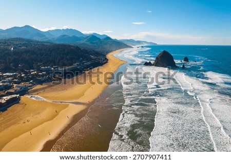 A breathtaking high-angle aerial view capturing the iconic Haystack Rock sea stack, the expansive sandy beach, and the Pacific Ocean coastline at Cannon Beach, Oregon