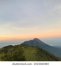 A breathtaking landscape view captured from the summit of Mount Merbabu. The scene features lush green valleys, rolling hills, and a panoramic vista of distant peaks surrounded by clouds - Powered by Shutterstock