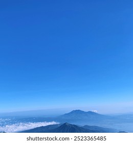 A breathtaking landscape view captured from the summit of Mount Merbabu. The scene features lush green valleys, rolling hills, and a panoramic vista of distant peaks surrounded by clouds - Powered by Shutterstock