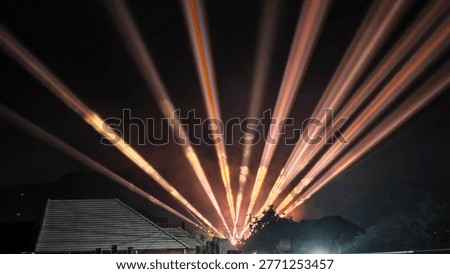 A breathtaking laser light show projects numerous bright beams into the dark night sky, creating a dynamic and colorful display. The powerful lights cut through the darkness, forming an impressive visual spectacle.