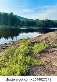 Breathtaking mountain peak and tree view. North South Lake Campground in the Catskill Mountains. Serene summer evening. Clear blue sky reflects over lake. Low tide water level due to dam rebuilding.  
