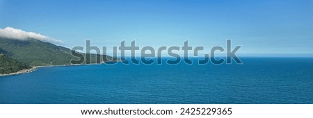 Breathtaking panoramic aerial view of a lush green coastal landscape meeting the calm blue sea under a clear sky, symbolizing tranquility and natural beauty