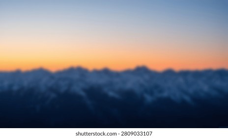 A breathtaking panoramic view of a mountain range blanketed in soft clouds during a vibrant sunrise, with the sky transitioning from deep blue to warm orange.