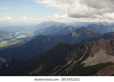 Breathtaking panoramic view of a mountain range with dramatic peaks, deep valleys, and a winding turquoise river under towering clouds. Scenic alpine landscape captured from a high vantage point, showcasing the grandeur of nature.