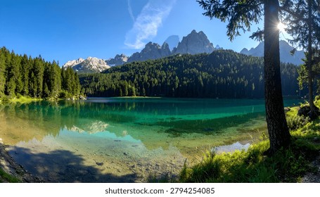 A breathtaking panoramic view of a pristine emerald lake reflecting the surrounding pine forest and towering mountains under a clear blue sky.