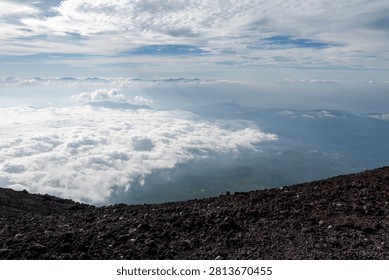 A breathtaking panoramic view from the summit of Mount Fuji, Japan's highest and most iconic volcano. The image captures the rugged volcanic crater, rocky ridges, winding hiking trails, and dramatic landscape above the clouds beneath a brilliant blue sky. This spectacular scene showcases the natural beauty and geological significance of Mount Fuji, a UNESCO World Heritage Site and one of Japan's most famous travel destinations. Ideal for themes of adventure, hiking, volcanic landscapes, nature, travel, and outdoor exploration.