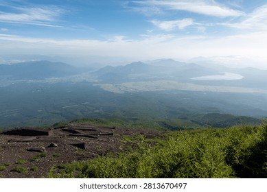 A breathtaking panoramic view from the summit of Mount Fuji, Japan's highest and most iconic volcano. The image captures the rugged volcanic crater, rocky ridges, winding hiking trails, and dramatic landscape above the clouds beneath a brilliant blue sky. This spectacular scene showcases the natural beauty and geological significance of Mount Fuji, a UNESCO World Heritage Site and one of Japan's most famous travel destinations. Ideal for themes of adventure, hiking, volcanic landscapes, nature, travel, and outdoor exploration.