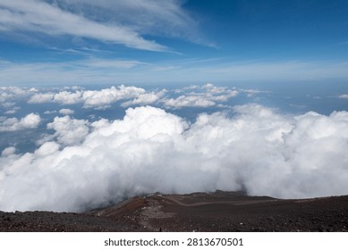 A breathtaking panoramic view from the summit of Mount Fuji, Japan's highest and most iconic volcano. The image captures the rugged volcanic crater, rocky ridges, winding hiking trails, and dramatic landscape above the clouds beneath a brilliant blue sky. This spectacular scene showcases the natural beauty and geological significance of Mount Fuji, a UNESCO World Heritage Site and one of Japan's most famous travel destinations. Ideal for themes of adventure, hiking, volcanic landscapes, nature, travel, and outdoor exploration.