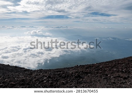 A breathtaking panoramic view from the summit of Mount Fuji, Japan's highest and most iconic volcano. The image captures the rugged volcanic crater, rocky ridges, winding hiking trails, and dramatic landscape above the clouds beneath a brilliant blue sky. This spectacular scene showcases the natural beauty and geological significance of Mount Fuji, a UNESCO World Heritage Site and one of Japan's most famous travel destinations. Ideal for themes of adventure, hiking, volcanic landscapes, nature, travel, and outdoor exploration.