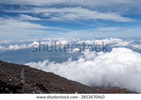 A breathtaking panoramic view from the summit of Mount Fuji, Japan's highest and most iconic volcano. The image captures the rugged volcanic crater, rocky ridges, winding hiking trails, and dramatic landscape above the clouds beneath a brilliant blue sky. This spectacular scene showcases the natural beauty and geological significance of Mount Fuji, a UNESCO World Heritage Site and one of Japan's most famous travel destinations. Ideal for themes of adventure, hiking, volcanic landscapes, nature, travel, and outdoor exploration.