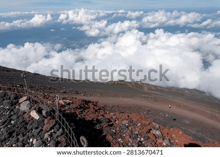 A breathtaking panoramic view from the summit of Mount Fuji, Japan's highest and most iconic volcano. The image captures the rugged volcanic crater, rocky ridges, winding hiking trails, and dramatic landscape above the clouds beneath a brilliant blue sky. This spectacular scene showcases the natural beauty and geological significance of Mount Fuji, a UNESCO World Heritage Site and one of Japan's most famous travel destinations. Ideal for themes of adventure, hiking, volcanic landscapes, nature, travel, and outdoor exploration.