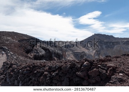 A breathtaking panoramic view from the summit of Mount Fuji, Japan's highest and most iconic volcano. The image captures the rugged volcanic crater, rocky ridges, winding hiking trails, and dramatic landscape above the clouds beneath a brilliant blue sky. This spectacular scene showcases the natural beauty and geological significance of Mount Fuji, a UNESCO World Heritage Site and one of Japan's most famous travel destinations. Ideal for themes of adventure, hiking, volcanic landscapes, nature, travel, and outdoor exploration.