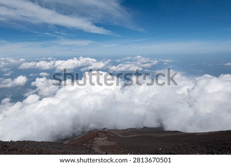 A breathtaking panoramic view from the summit of Mount Fuji, Japan's highest and most iconic volcano. The image captures the rugged volcanic crater, rocky ridges, winding hiking trails, and dramatic landscape above the clouds beneath a brilliant blue sky. This spectacular scene showcases the natural beauty and geological significance of Mount Fuji, a UNESCO World Heritage Site and one of Japan's most famous travel destinations. Ideal for themes of adventure, hiking, volcanic landscapes, nature, travel, and outdoor exploration.