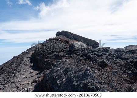 A breathtaking panoramic view from the summit of Mount Fuji, Japan's highest and most iconic volcano. The image captures the rugged volcanic crater, rocky ridges, winding hiking trails, and dramatic landscape above the clouds beneath a brilliant blue sky. This spectacular scene showcases the natural beauty and geological significance of Mount Fuji, a UNESCO World Heritage Site and one of Japan's most famous travel destinations. Ideal for themes of adventure, hiking, volcanic landscapes, nature, travel, and outdoor exploration.