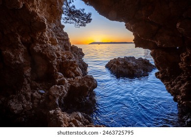 A breathtaking photograph capturing the view of a sunset through the opening of a coastal cave. The image showcases the rugged rocks framing the serene ocean - Powered by Shutterstock