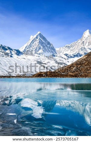 A breathtaking scene from Tibet, showcasing the tranquil beauty of a frozen alpine lake surrounded by towering snow-covered mountains. The sharp reflection of the mountains on the still, icy water add