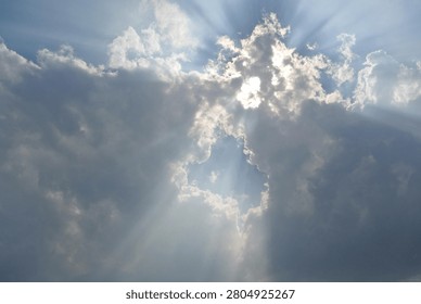 A breathtaking shot of dramatic sunbeams breaking through dramatic gray clouds in a blue sky. Beautiful natural crepuscular rays or God's rays effect beaming through cloud gap, perfect for spiritual, hope, and inspirational concepts.