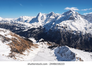 Breathtaking snowy peaks and rugged terrain of Murren ski resort in Switzerland. Snow covered slopes, ski lift cables, deep valley, forest patches, majestic Swiss Alps view under a clear blue sky. - Powered by Shutterstock
