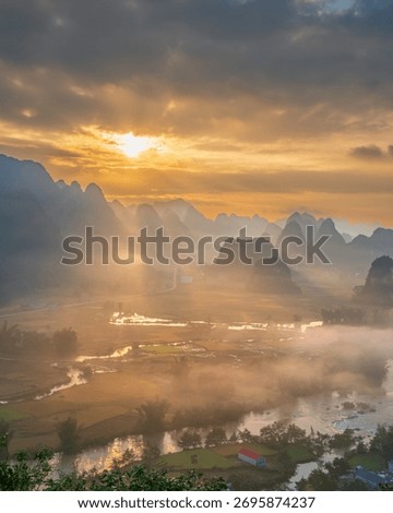 Breathtaking sunrise with dramatic sun rays piercing through the mist and clouds over the rice fields and karst mountains in Ngoc Con Valley, Cao Bang, Vietnam.