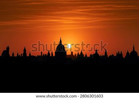 A breathtaking sunset casts a warm orange glow over the iconic London skyline, creating dramatic silhouettes of famous buildings.